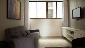 Ein Wohnzimmer mit einer Couch, einem an der Wand befestigten Fernseher und einem Fenster mit Vorhängen.