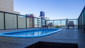 Ein Poolbereich auf dem Dach mit Blick auf die Skyline der Stadt, einer Holzterrasse und Liegestühlen.