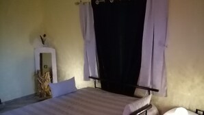 A bedroom with a bed, a nightstand, a mirror, and a window with curtains.