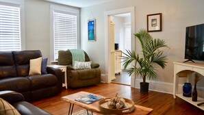 Una sala de estar con un sofá de cuero, un sillón verde, una mesa de centro con una revista, una palmera en maceta y un televisor sobre un mueble.