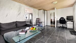 A modern living room with a glass coffee table, a grey sofa, and a dining area with chairs.