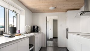 A modern kitchen with white cabinetry, a stainless steel range hood, and a black coffee machine.
