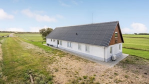 A modern, single-story building with a sloped roof, situated in a rural setting with expansive green fields.