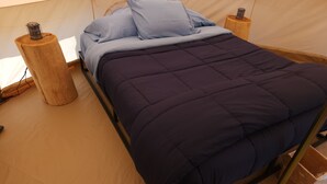 Une tente avec un lit, deux lanternes et un tabouret en bois.
