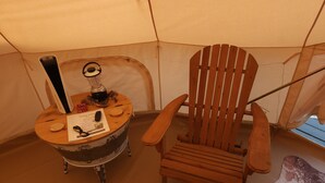 L’intérieur d’une tente, avec une chaise en bois et une table de style vintage sur laquelle se trouvent une lampe, une télécommande et un menu.