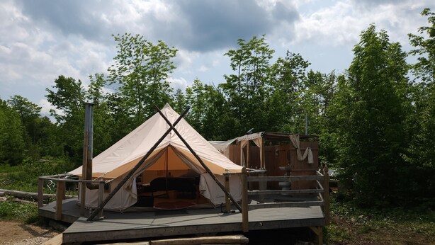 Une tente dotée d’une terrasse en bois et d’une petite structure en bois attenante.