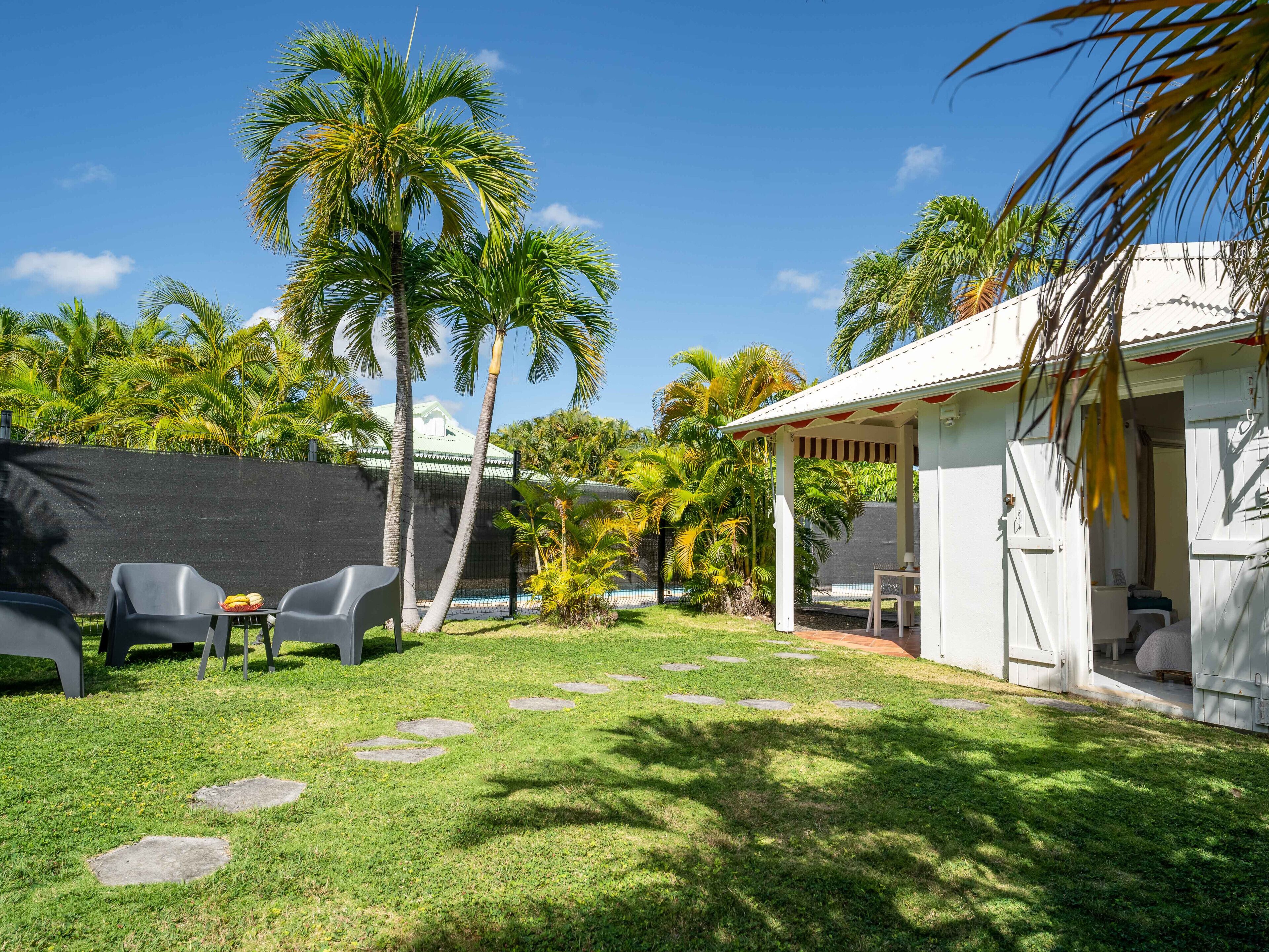 Un jardin avec un bâtiment blanc, des palmiers et un espace salon abrité.