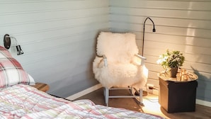 A cozy bedroom with a fluffy chair, a bedside lamp, a bedside table with a plant, and a bed with a striped blanket. - Awesome home in Laukvik with kitchen (Laukvik)