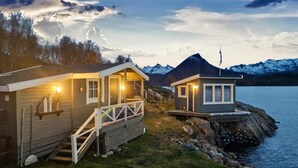 Two wooden cabins with external lighting, a staircase, and a view of a lake and mountains. - Awesome home in Laukvik with kitchen (Laukvik)