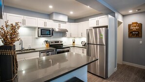A modern kitchen with white cabinets, stainless steel appliances, and a black countertop. - Al's Escape by Revelstoke Vacations (Revelstoke)
