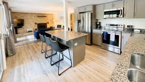 Una cocina moderna con una isla central, electrodomésticos de acero inoxidable y un comedor con taburetes de bar.