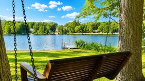 Un banco de madera con cadenas, ubicado en un parque con un lago y árboles al fondo.