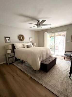 Cozy retreat with a large bed, nightstand, and bedside table, featuring a ceiling fan and a window with an outdoor view.