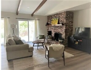 Cozy living room with a brick-patterned fireplace, television, and seating areas.