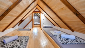 Une chambre confortable située dans les combles, avec des poutres apparentes, deux lits et une petite salle de bain.