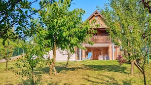 Une maison en bois à deux étages, dotée d’un balcon, entourée d’arbres et d’une pelouse verdoyante.