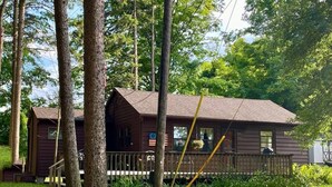 A cabin with a porch, surrounded by lush greenery and tall trees.