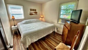 A bedroom with a bed, a desk with a chair, a television, and a window with blinds.