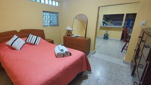 Un dormitorio con cama, mesita de noche, cómoda, espejo y ventana con cortinas estampadas.
