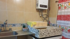 Cocina compacta con lavamanos, calentador de agua y un armario rojo con dos cajones.