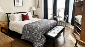 A neatly arranged bedroom with a bed, bedside table, lamp, and a small round table with a chair. - Historic District, Downtown, STE 1 (Rapid City)
