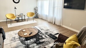 A living room with a round coffee table, two yellow chairs, a bookshelf, a flat-screen TV, and a ceiling fan. - Historic District, Downtown, STE 1 (Rapid City)