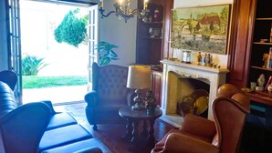 A well-lit living room with a fireplace, a comfortable sofa, a table with a lamp, and a bookshelf. - Moradia Entre o mar e a ria (Gafanha da Nazaré)