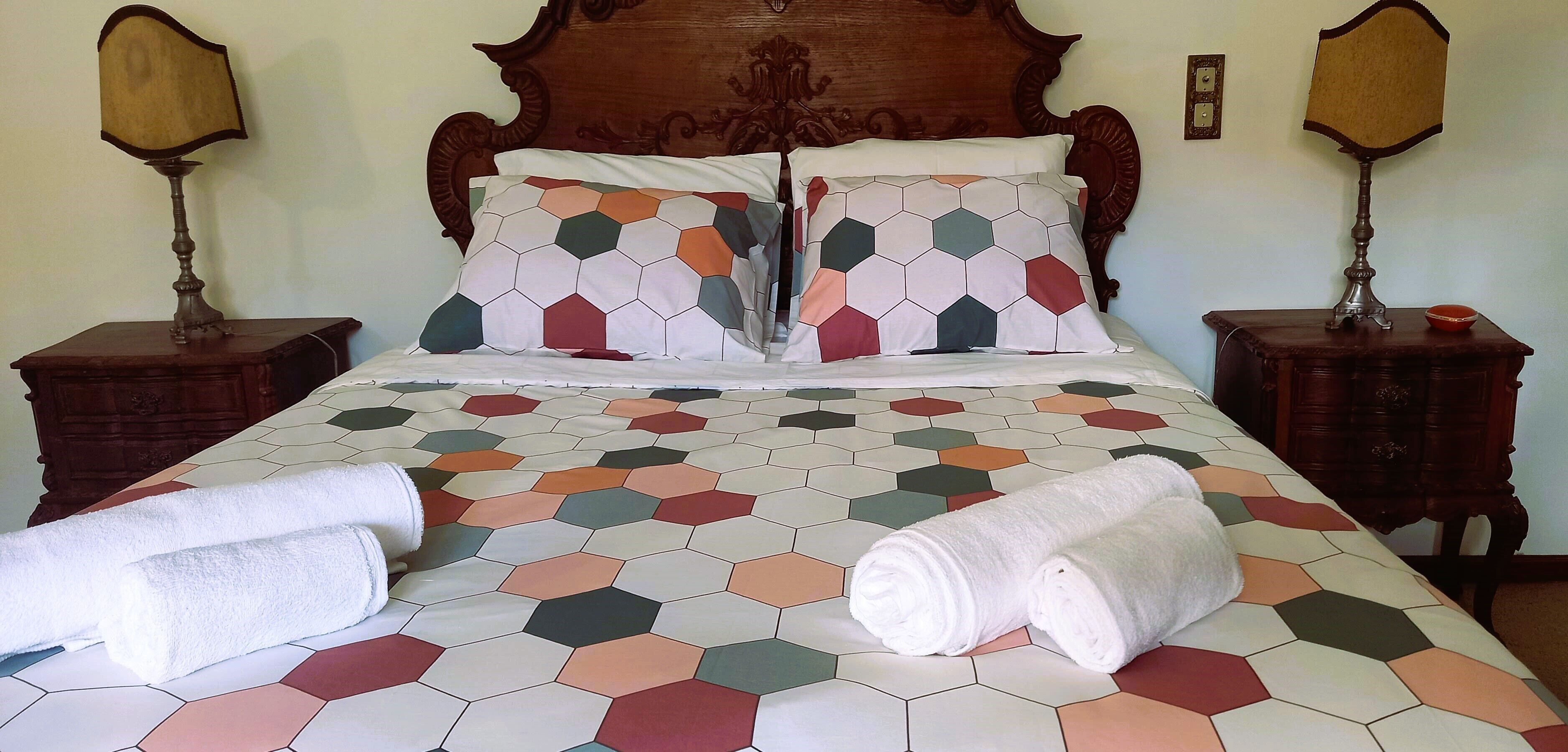 A neatly made bed with a geometric-patterned bedspread, two matching pillows, and two bedside tables with lamps.