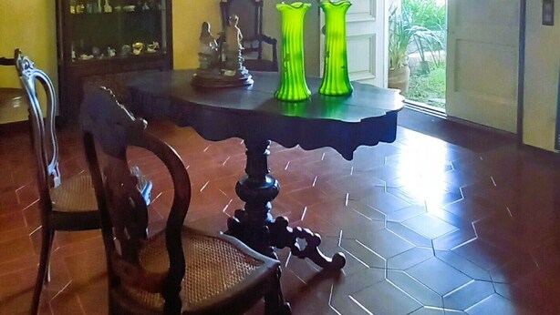A dining area with a hexagonal tile floor, a wooden dining table, two chairs, a chandelier, and a door leading outside. - Moradia Entre o mar e a ria (Gafanha da Nazaré)