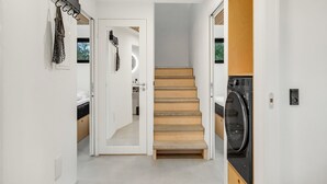 A modern interior with a wooden staircase, a washing machine, and a kitchen area.