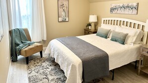A bedroom with a bed, a chair, a nightstand, a lamp, and a painting on the wall. - Historic District, Downtown, STE 3 (Rapid City)