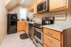 A compact kitchen with wooden cabinets, a black refrigerator, a stove, and a microwave. - Historic District, Downtown, STE 3 (Rapid City)