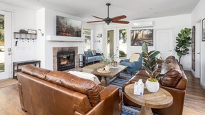 A modern living room with leather sofas, a fireplace, a ceiling fan, and large windows. - Clockers House at Galway - 3 bedroom, 3 bath luxury home on-site of Galway Downs (Temecula)