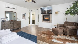 A modern bedroom with a large bed, a wooden dresser, a blue ottoman, a leather sofa, a fireplace, and a ceiling fan. - Clockers House at Galway - 3 bedroom, 3 bath luxury home on-site of Galway Downs (Temecula)