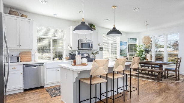 A modern kitchen with white cabinetry, a central island, bar stools, and a dining table. - Clockers House at Galway - 3 bedroom, 3 bath luxury home on-site of Galway Downs (Temecula)