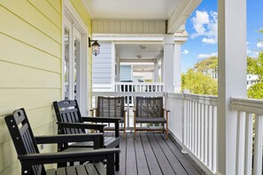 A porch with two chairs and a table, a white railing, and a view of a house in the background.