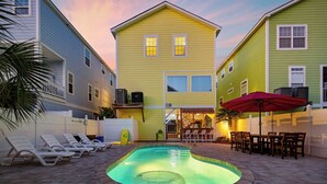 En swimmingpool med solstolar, ett rött parasoll och ett hus med en balkong.