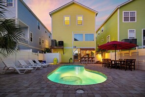 A swimming pool with lounge chairs, a red umbrella, and a house with a balcony.