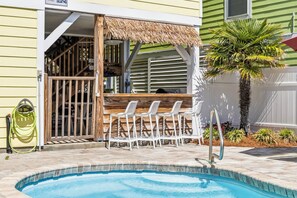 A pool area with a thatched roof seating area, a pool ladder, and a hose.