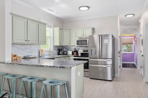 A modern kitchen with granite countertops, stainless steel appliances, and light green cabinetry.