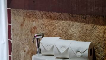 A bathroom with a stone wall, a white toilet, and a metal faucet.