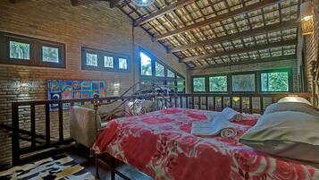 A spacious room with a large bed, a wooden ceiling, and multiple windows offering views of the outdoors.