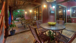 A covered patio area with wooden furniture, potted plants, and a table with a banana centerpiece. - Casa na Serra de Mulungu por Carpediem (Mulungu)