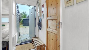 A narrow hallway with a wooden door, a bench, and a small outdoor area with a gravel path and a building in the background.