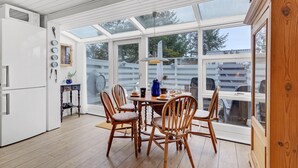 A conservatory with a dining table and chairs, a white refrigerator, and a wooden cabinet.