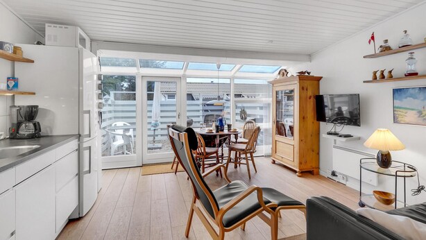 A modern kitchen with a dining area, large windows, and a TV.