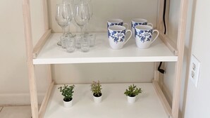 Una estantería blanca con una cafetera, dos tazas azules y tres pequeñas macetas.