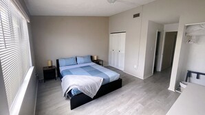 Un dormitorio con cama, armario, mesita de noche y ventana con persianas.