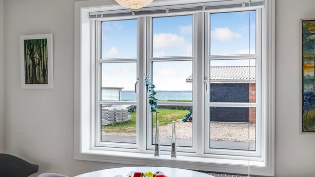 A room with a large window offering a view of the sea and a grassy area. There is a table with a fruit bowl and salt shakers. - Amazing home in Tranekær with WiFi (Tranekær)