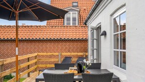 An outdoor patio with a table and chairs, a wooden fence, and a red-tiled roof in the background. - Amazing home in Tranekær with WiFi (Tranekær)